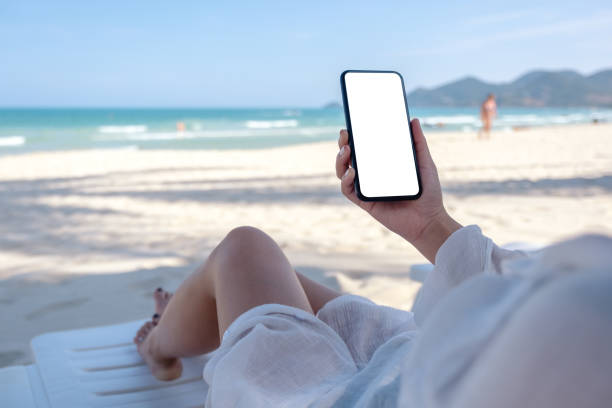 istock a woman holding white mobile phone with blank desktop screen while laying down on beach chair 1148979415