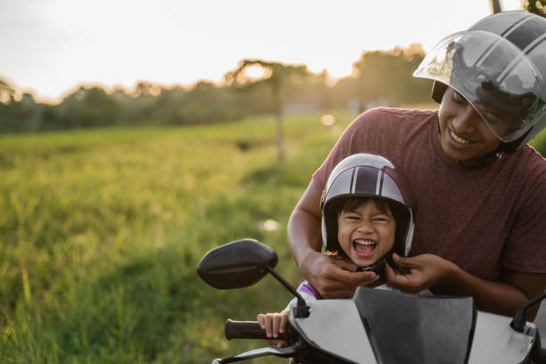 daddy help her daughter to fasten the helmet while riding a motorcycle scooter