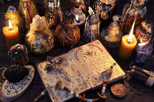 Ancient witch book with magic spell, black candles and decorated bottles. Halloween, esoteric and occult background. No foreign text, all symbols on pages are fictional.