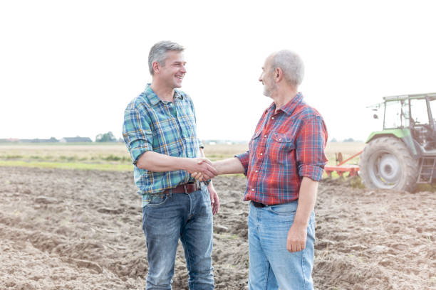istock Smiling farmers shaking hands while standing on field at farm 1148984451