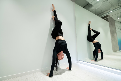 Stand near mirror. Dark-haired active woman feeling good while doing arm stand near mirror