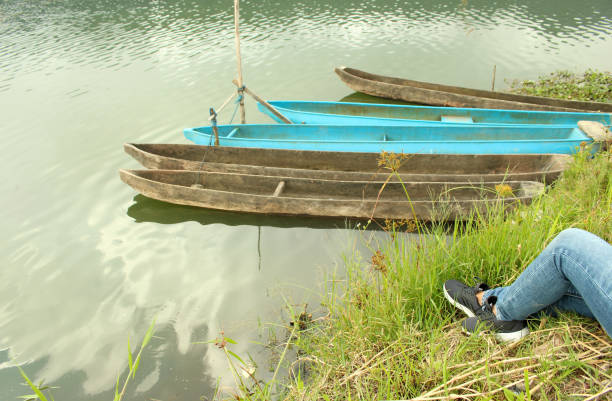 Tranquility lake scene with natural wooden fishing boats and the legs of young woman in the edge of the lake, enjoying the view.  Weekend relaxation concept.
