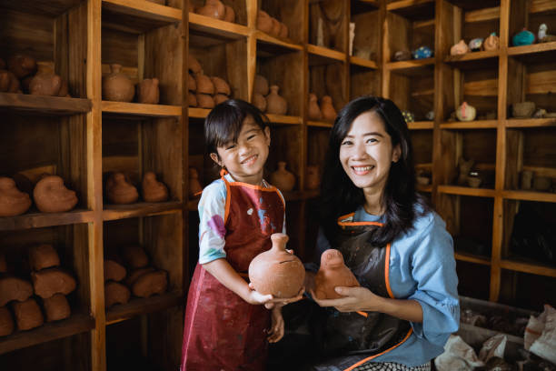 mother and daughter wearing apron and holding pottery goods made from clay
