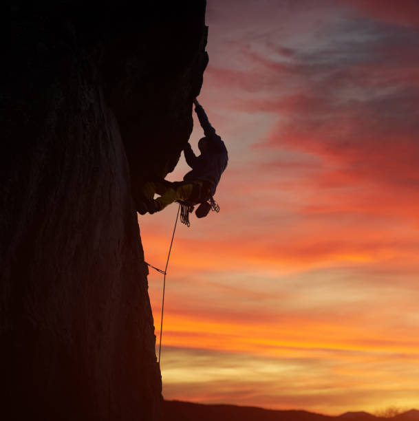 istock Silhouette male climber rock climbing pulling up with both hands. Sunset orange sky on background. Low angle. Copy space 1148998530