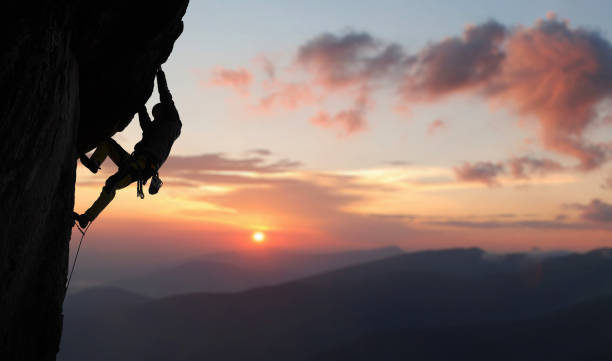 escalade mâle tirant vers le haut, faisant la prochaine étape atteignant le dessus. vue latérale. vue panoramique sur la montagne et le coucher du soleil. espace de copie - climbing rock climbing rock mountain climbing photos et images de collection