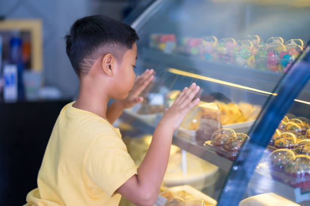 Asian kid boy waiting at bakery shop and choosing bakery that him like stock photo