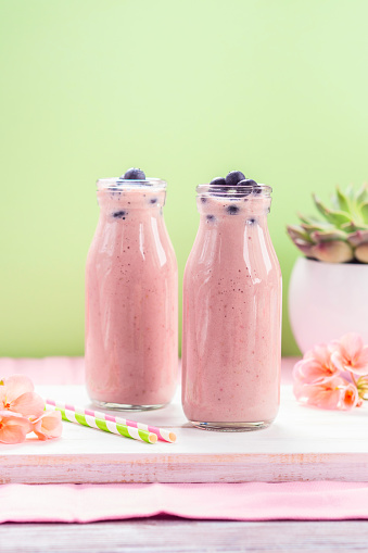 Pink milk shake in glass bottles topped with blueberries. Pink flowers and colorful straws.