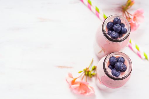 Pink milk shake in glass bottles topped with blueberries. Pink flowers and colorful straws. Top view