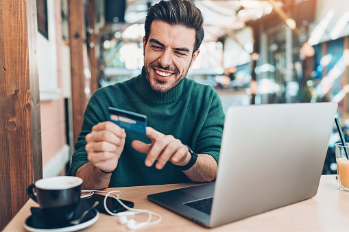 Smiling young man with laptop and credit card in cafe