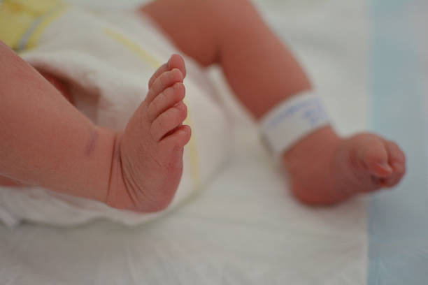 CLOSE-UP NEWBORN BABY AT THE HOSPITAL WITH IDENTIFY TAG ON FEET AND DIAPER. CLOSE-UP NEWBORN BABY AT THE HOSPITAL WITH IDENTIFY TAG ON FEET AND DIAPER. legs apart stock pictures, royalty-free photos & images