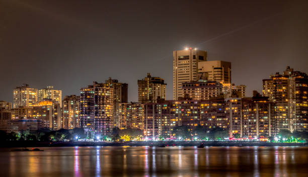 mesmerizing photo of colaba skyline at night, as seen from nariman point of marine drive.  buildings, roadside and night market light reflections may be seen in calm arabian sea, is like cherry on top - boston skyline night city imagens e fotografias de stock