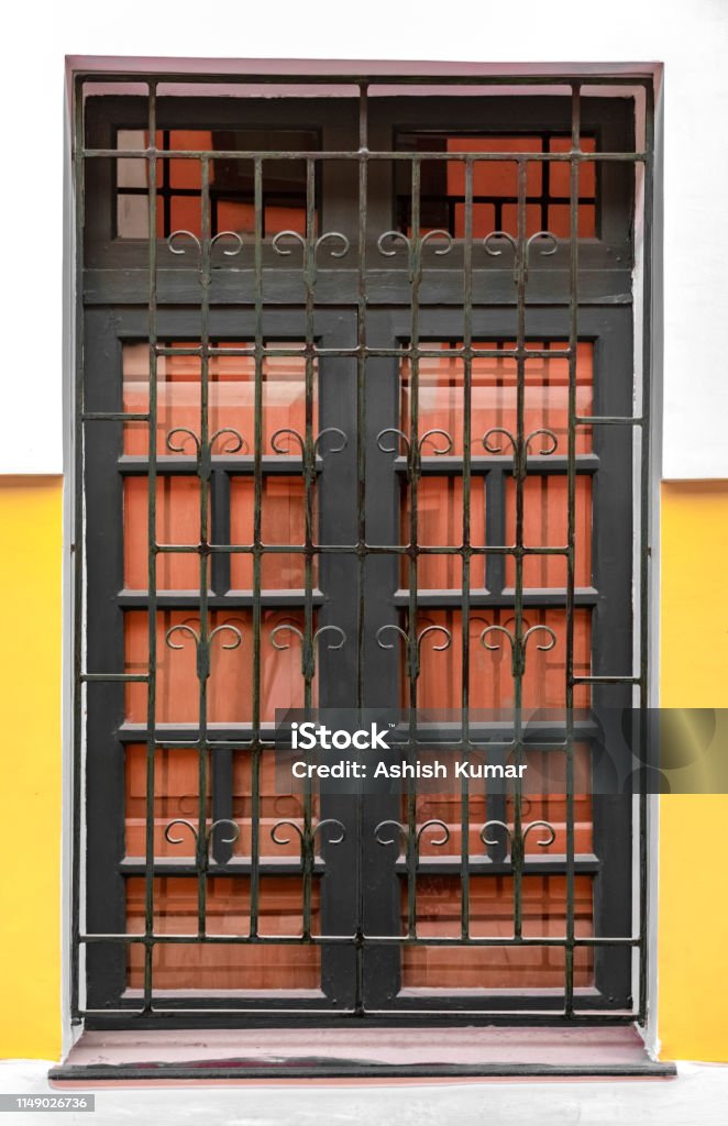 Very Beautiful Corinthian Style Big Window, having Iron Bars with patterns and Wooden Gate attached to it. A Typical Colonian Era Roman Architecture. - Image Amazing Corinthian Style Big Windows in the Goa city of India. Such windows in almost every house of the traditional Goa depicts the impact of Portuguese architecture and culture on Goan homes. These big windows are perfect for the good ventilation in the room, and is made up of wood and iron bars. Ancient Stock Photo