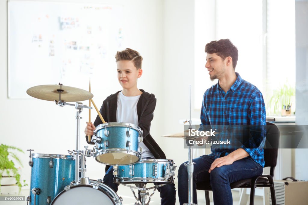 Music teacher explaining boy to play drums Male music teacher explaining little drummer. Pre-adolescent boy is listening to mid adult instructor. They are practicing in conservatory. Child Stock Photo