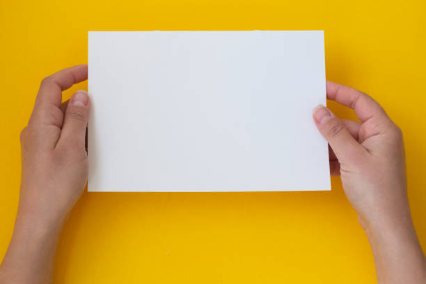 istock Hands holding blank white, empty paper isolated on yellow with copy space 1149038339