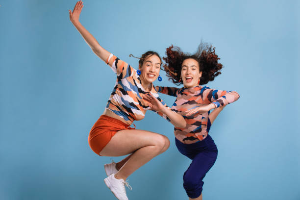 Jumping and Dabbibng Two sisters jumping in fun positions laughing and looking at the camera in front of a blue studio background. dab dance stock pictures, royalty-free photos & images