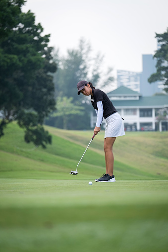 Surface level of female golfer lining up her putt. Full length of teenage girl is playing golf on field. She is in sports clothing.