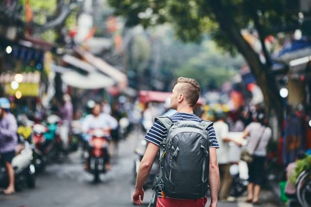 Traveler walking on busy street. Rear view of young man with backpack in Hanoi, Vietnam.