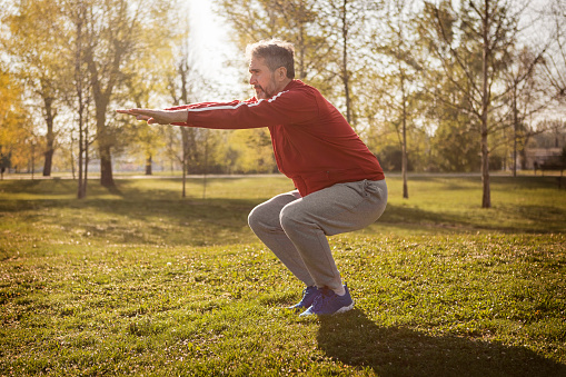 Senior jogger doing squats in public park