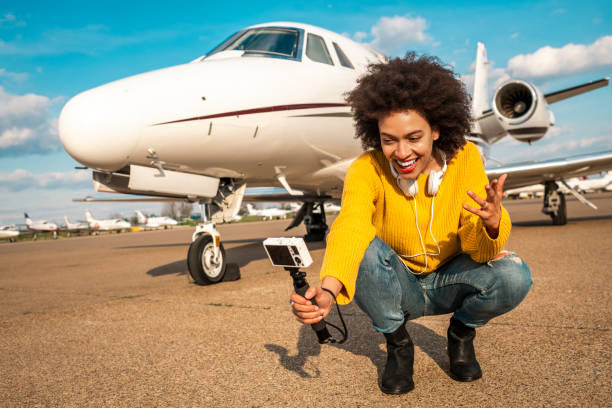 joven bonita chica vlogger haciendo contenido al lado de un jet privado estacionado en una pista de aterrizaje del aeropuerto - status symbol audio fotografías e imágenes de stock