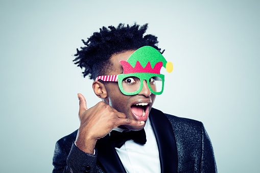 Close up of a excited young african man wearing funny christmas mask making a call me gesture on gray background