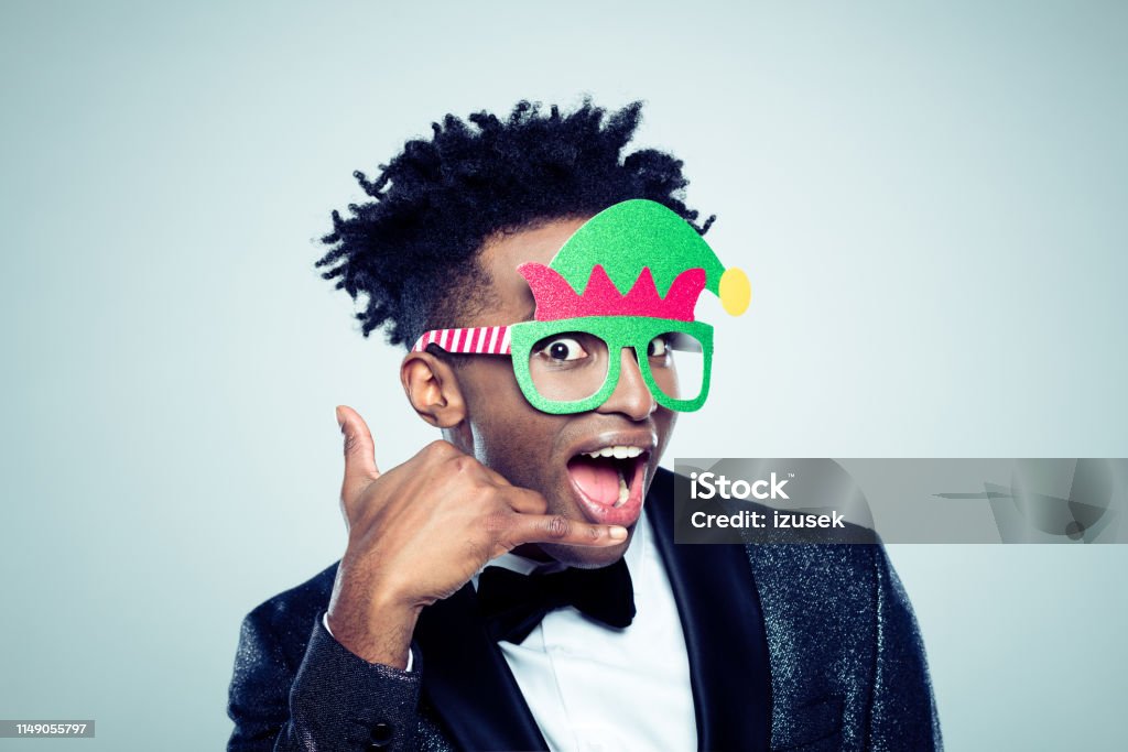 Call me for the christmas party Close up of a excited young african man wearing funny christmas mask making a call me gesture on gray background Christmas Stock Photo