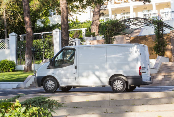 White van is parked in shade of trees on pavement at entrance to sanatorium surrounded by white fence.