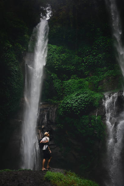 istock Happy man backpacker enjoying amazing tropical waterfall on background nature landscape. Travel Lifestyle and success concept vacations into the wild nature on background mountain and rainforest 1149060689