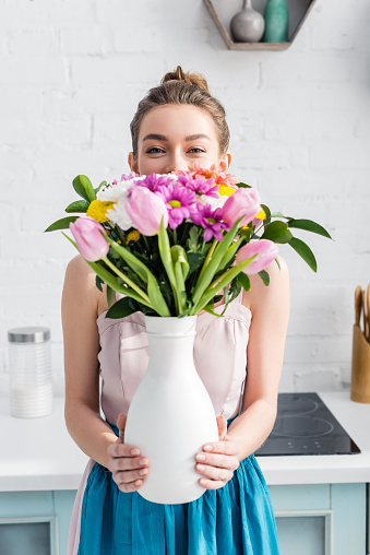 pretty girl with obscure face hiding behind bouquet of wildflowers in vase