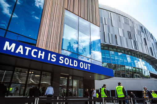 London, UK - 12 May, 2019: color image depicting teams of security workers wearing high-visibilty jackets working outside the brand new modern architecture of the Tottenham Hotspur stadium in north London, UK. It is the day of an English Premier League match (Tottenham v Everton) and the security staff are waiting to inspect and frisk many thousands of football supporters. Room for copy space.