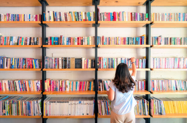 asiatiska kvinnor plockar upp böcker på bok hyllan. att förbereda sig för att återvända till skolan - library bildbanksfoton och bilder