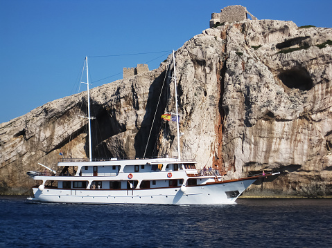 White cruise sailing ship near the huge cliff in national park Kornati in croatia at sunny afternoon