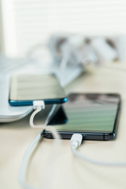 Different mobile phones connected to charger Desktop with smart phones connected to electrical cahrger mobile phone charger stock pictures, royalty-free photos & images