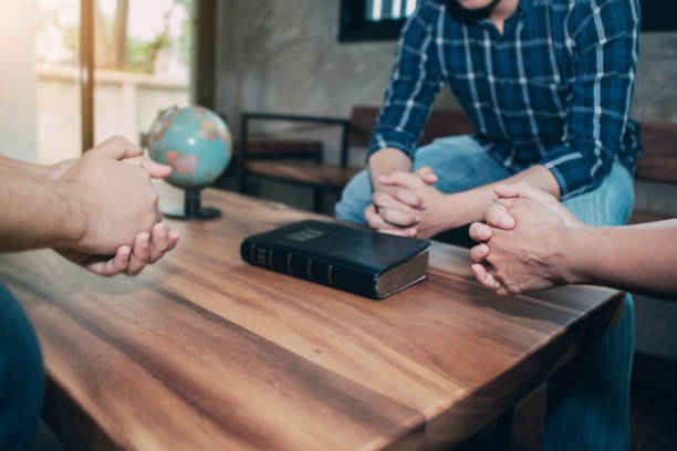 three Christian friends praying for world mission Christian group are praying around wooden table with holy blurred bible and world globe, christian background , pray for the world concept minister clergy photos stock pictures, royalty-free photos & images