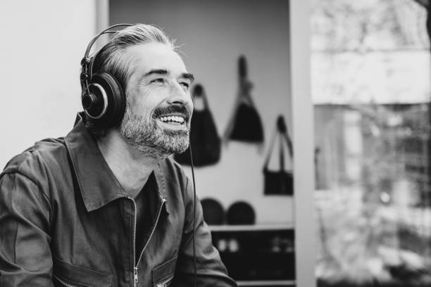 enjoy the music handsome smiling bearded man in overall with headphones sitting outdoors and listening black and white headphones stock pictures, royalty-free photos & images
