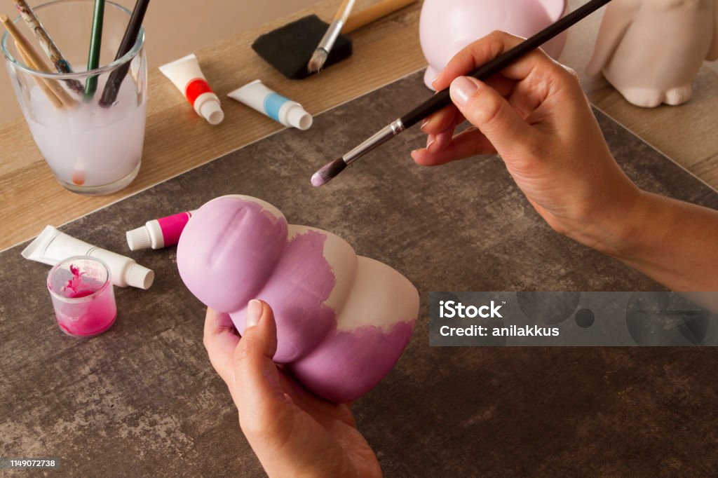 High Angle View of Adult Woman Hands Painting Coin Banks Top view shooting of an adult woman hands painting clay coin banks 40-44 Years Stock Photo