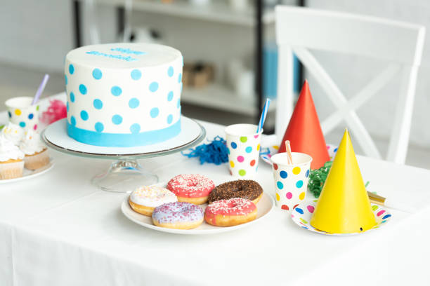 istock delicious birthday cake with cupcakes, doughnuts and paper cups on festive table 1149074801