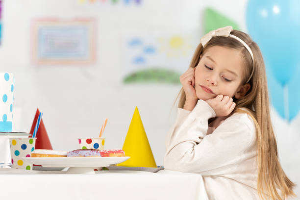 istock upset kid sitting at table with donuts and party caps during birthday celebration 1149074821