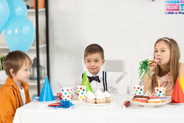 istock kids sitting at table with cupcakes and party horns during birthday celebration 1149074849