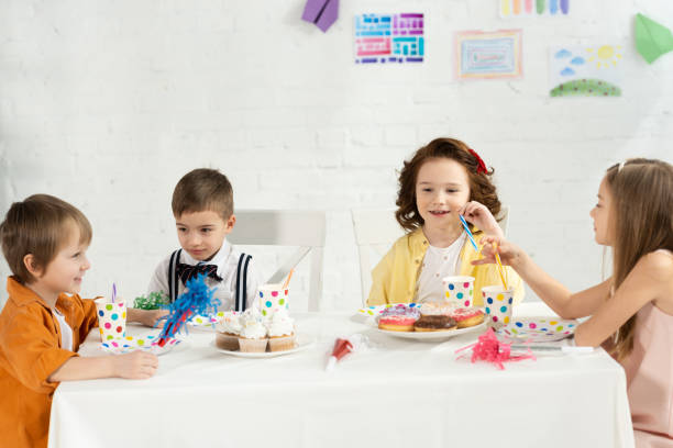 istock kids sitting at table with cupcakes and party horns during birthday celebration 1149074855