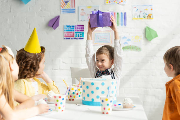 istock happy boy holding present while sitting at table with friends during birthday party celebration 1149074944