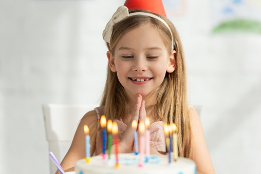 selective focus of adorable kid with birthday cake doing please gesture during party