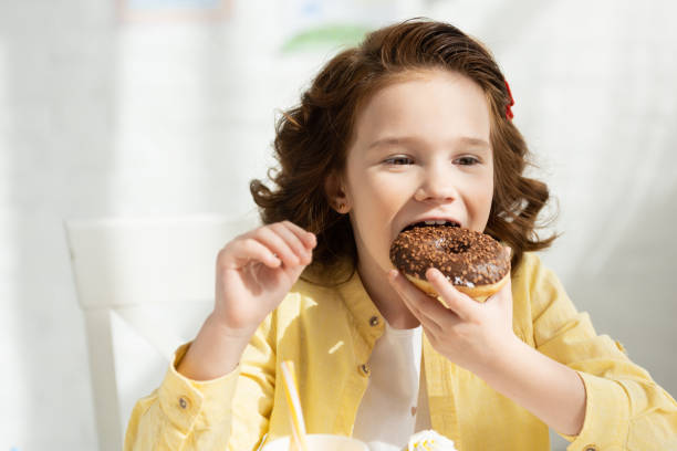 istock adorable kid in yellow eating delicious doughnut at table 1149075643