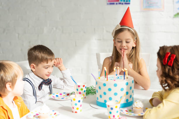 istock adorable kid doing please gesture and making wish while sitting at table with friends during birthday party celebration 1149075666