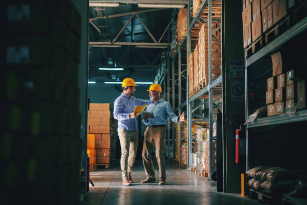 istock Two successful business partners in formal wear discussing about sales while standing in warehouse. 1149079285