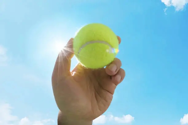 Man holding and serving a yellow tennisball against blue sky. Sports, competition and fitness concept.