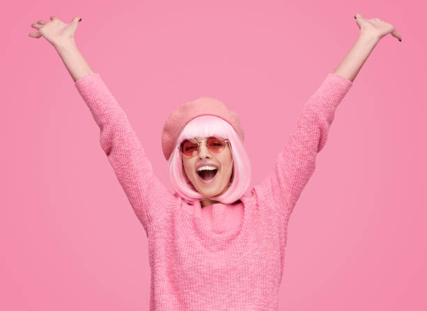 Lovely young lady in trendy beret and sunglasses screaming and raising hands while standing on pink background. Girl having a vacation
