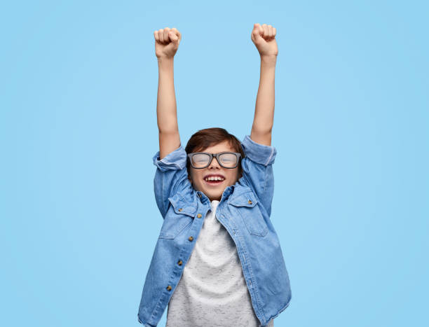 Happy kid in glasses holding hands up Cheerful little boy in eyeglasses with arms raised looking with smile at camera celebrating win . School kid winner cheerful children stock pictures, royalty-free photos & images