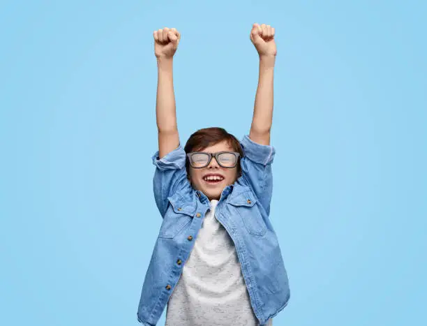 Photo of Happy kid in glasses holding hands up
