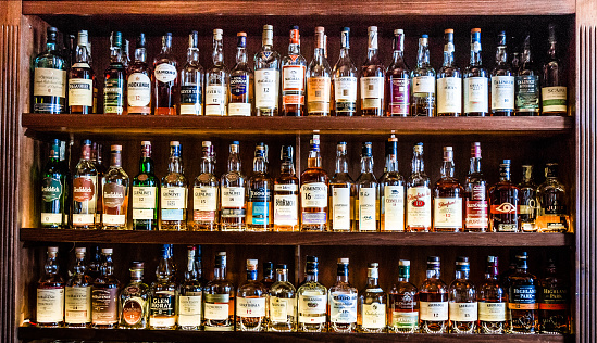 London, UK - 10 May, 2019: Color image depicting a huge selection of different malt Scotch whisky bottles in a row and displayed on wooden shelves at a bar in London, UK. The whisky is mainly Scottish single malt and comes from a range of different distilleries. Room for copy space.