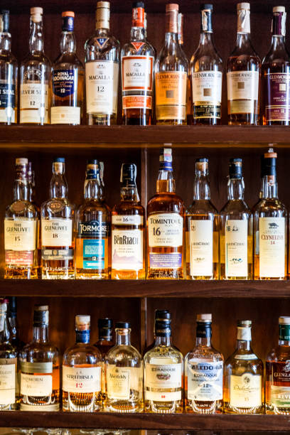 London, UK - 10 May, 2019: Color image depicting a huge selection of different malt Scotch whisky bottles in a row and displayed on wooden shelves at a bar in London, UK. The whisky is mainly Scottish single malt and comes from a range of different distilleries. Room for copy space.